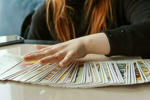 TVER, RUSSIA - FEBRUARY 11, 2023. Tarot cards, Tarot card divination, esoteric background. A woman makes a layout on the cards at the table. Divination, predictions on tarot cards. photo