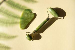 Jade Gua sha scraper and facial massager on beige background. photo