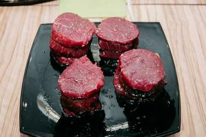 Raw beef meat for steak preparation. Raw beef sliced, preparation of meat for cooking steak at the culinary master class. Raw meat on a black plate. photo