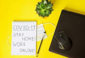 Top view of a desktop with laptops, a marker, and a laptop. Text Covid-19, stay at home, WORK ONLINE. Work from home, protection from coronavirus during the quarantine period. Yellow background. photo