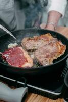 Cocinando filetes en un cacerola. Cocinando carne de vaca a el culinario Maestro clase. el manos de el cocinero en negro guantes. foto