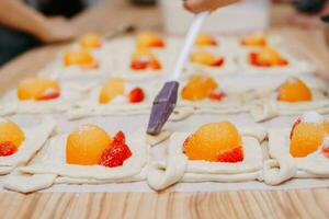 Preparing a dessert at a cooking master class. Baskets with peaches and strawberries, home cooking. Close-up, selective focus. Pastries, pies with peaches from puff pastry. photo