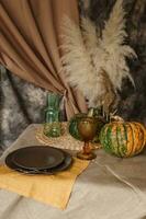 Autumn interior. A table covered with dishes, pumpkins, a relaxed composition of Japanese pampas grass. Interior in the photo Studio. Close - up of a decorated autumn table.