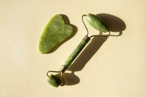 Jade Gua sha scraper and facial massager on beige background. photo