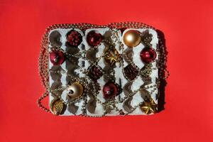 Christmas tree toys in the egg tray on a red background. Top view. The concept of New Year's holidays and Christmas. Red and gold colors. photo