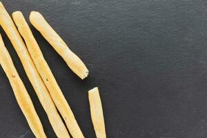 Fresh Italian Grissini Breadsticks served on black background. Dry baked bread with olive pieces photo