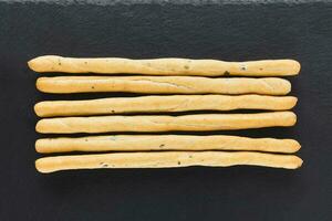 Fresh Italian Grissini Breadsticks served on black background. Dry baked bread with olive pieces photo