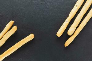 Fresh Italian Grissini Breadsticks served on black background. Dry baked bread with olive pieces photo