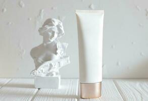 Cosmetic cream bottle and head statue on table, mockup photo