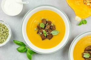 Seasonal autumn roasted pumpkin and carrot soup with cream and rye bread croutons on a light concrete background. Top view. photo