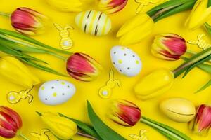 Easter floral background, various eggs, bunnies and colorful tulips on yellow background. Top view. photo