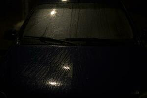 Raindrops on car in dark. Car at night in parking lot. Car in rain. photo