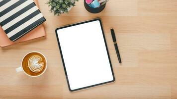 de madera escritorio lugar de trabajo con blanco pantalla tableta, bolígrafo, cuaderno y taza de café, parte superior ver plano laico con Copiar espacio. foto