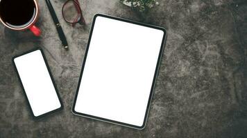 Dark office desk workplace with blank screen tablet and smartphone, laptop, keyboard, pen, eyeglass and notebook, Top view flat lay. photo