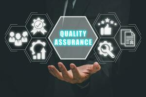 Quality Assurance concept, Business hand holding Quality Assurance icon on virtual screen. photo