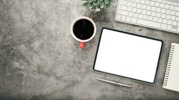 oficina escritorio lugar de trabajo con blanco pantalla tableta, bolígrafo, computadora portátil, teclado y taza de café, parte superior ver plano laico con Copiar espacio. foto