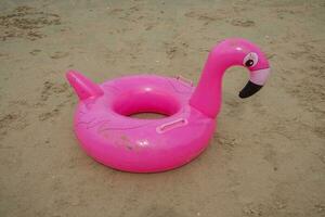 a pink flamingo-shaped buoy on the beach sand. Summer concept photo
