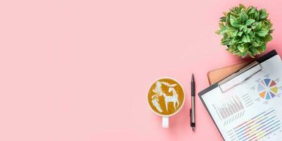 Office desk table with analysis chart or graph, pen, cup of coffee on pink background. Top view with copy space, Working desk table concept. photo