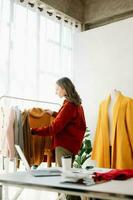 asiático Sastre mujer trabajando en ropa en sastrería taller. hermosa joven hembra Moda diseñador sonrisa y después éxito en estudio foto