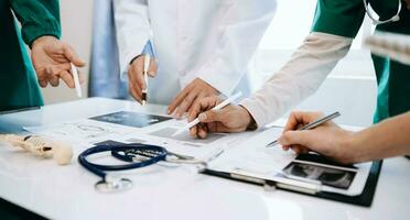 Medical team having a meeting with doctors in white lab coats and surgical scrubs seated at a desk discussing a patients working online using computers in the medical industry photo