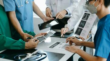 Medical team having a meeting with doctors in white lab coats and surgical scrubs seated at a table discussing a patients working online using computers in the medical industry photo