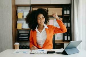 africano negocio mujer son Encantado y contento con el trabajo ellos hacer en su tableta, ordenador portátil y tomando notas a el oficina. foto