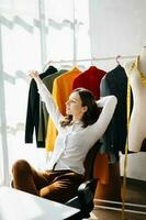 Caucasian young woman on desk in home office of fashion designer and holds tablet, laptop and smartphone. photo