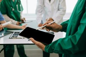 Medical team having a meeting with doctors in white lab coats and surgical scrubs seated at a desk discussing a patients working online using computers in the medical industry photo