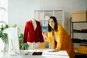 Fashion designer woman talking smart phone and using laptop with digital tablet computer in modern studio the clothes hanging on the racks photo