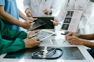 Medical team having a meeting with doctors in white lab coats and surgical scrubs seated at a table discussing a patients working online using computers in the medical industry photo