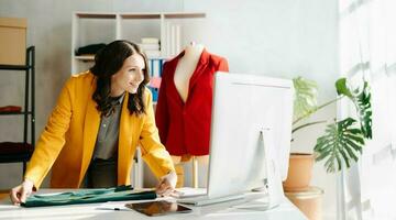 Caucasian young woman on desk in home office of fashion designer and holds tablet, laptop and smartphone. photo