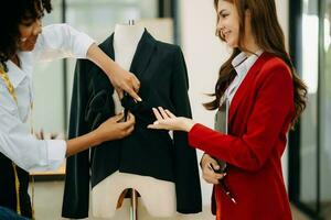 Pareja de Moda diseñadores trabajando con tela y ropa bocetos a el estudio lleno de sastrería herramientas y sostiene tableta y ordenador portátil. foto