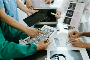 Medical team having a meeting with doctors in white lab coats and surgical scrubs seated at a table discussing a patients working online using computers in the medical industry photo