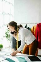 Caucasian young woman on desk in home office of fashion designer and holds tablet, laptop and smartphone. photo