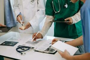 Medical team having a meeting with doctors in white lab coats and surgical scrubs seated at a desk discussing a patients working online using computers in the medical industry photo