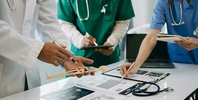 Medical team having a meeting with doctors in white lab coats and surgical scrubs seated at a desk discussing a patients working online using computers in the medical industry photo