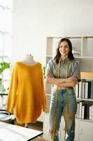 Fashion designer woman talking smart phone and using laptop with digital tablet computer in modern studio the clothes hanging on the racks photo