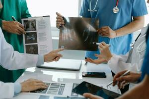 médico equipo teniendo un reunión con doctores en blanco laboratorio abrigos y quirúrgico matorrales sentado a un mesa que se discute un pacientes trabajando en línea utilizando ordenadores en el médico industria foto