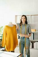 Caucasian young woman on desk in home office of fashion designer and holds tablet, laptop and smartphone. photo