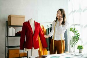 Caucasian young woman on desk in home office of fashion designer and holds tablet, laptop and smartphone. photo