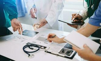 Medical team having a meeting with doctors in white lab coats and surgical scrubs seated at a desk discussing a patients working online using computers in the medical industry photo