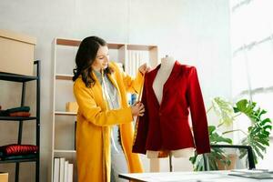 Fashion designer woman talking smart phone and using laptop with digital tablet computer in modern studio the clothes hanging on the racks photo