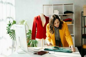 Caucasian young woman on desk in home office of fashion designer and holds tablet, laptop and smartphone. photo