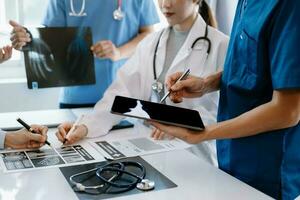 Medical team having a meeting with doctors in white lab coats and surgical scrubs seated at a table discussing a patients working online using computers in the medical industry photo