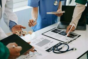Medical team having a meeting with doctors in white lab coats and surgical scrubs seated at a desk discussing a patients working online using computers in the medical industry photo
