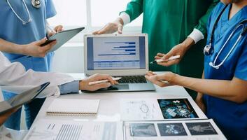 Medical team having a meeting with doctors in white lab coats and surgical scrubs seated at a table discussing a patients working online using computers in medical industry photo