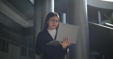 joven asiático mujer de negocios en traje trabajando en ordenador portátil a al aire libre cerca oficina foto