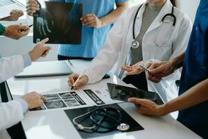 médico equipo teniendo un reunión con doctores en blanco laboratorio abrigos y quirúrgico matorrales sentado a un mesa que se discute un pacientes trabajando en línea utilizando ordenadores en el médico industria foto