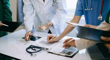 Medical team having a meeting with doctors in white lab coats and surgical scrubs seated at a desk discussing a patients working online using computers in the medical industry photo