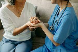 Medical doctor holing senior patient's hands and comforting her at home photo